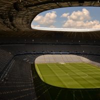 An empty sports stadium with a well-maintained soccer field under a cloudy sky