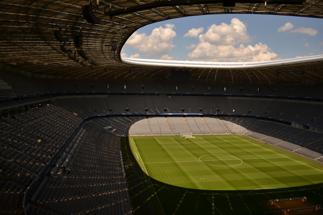 An empty sports stadium with a well-maintained soccer field under a cloudy sky